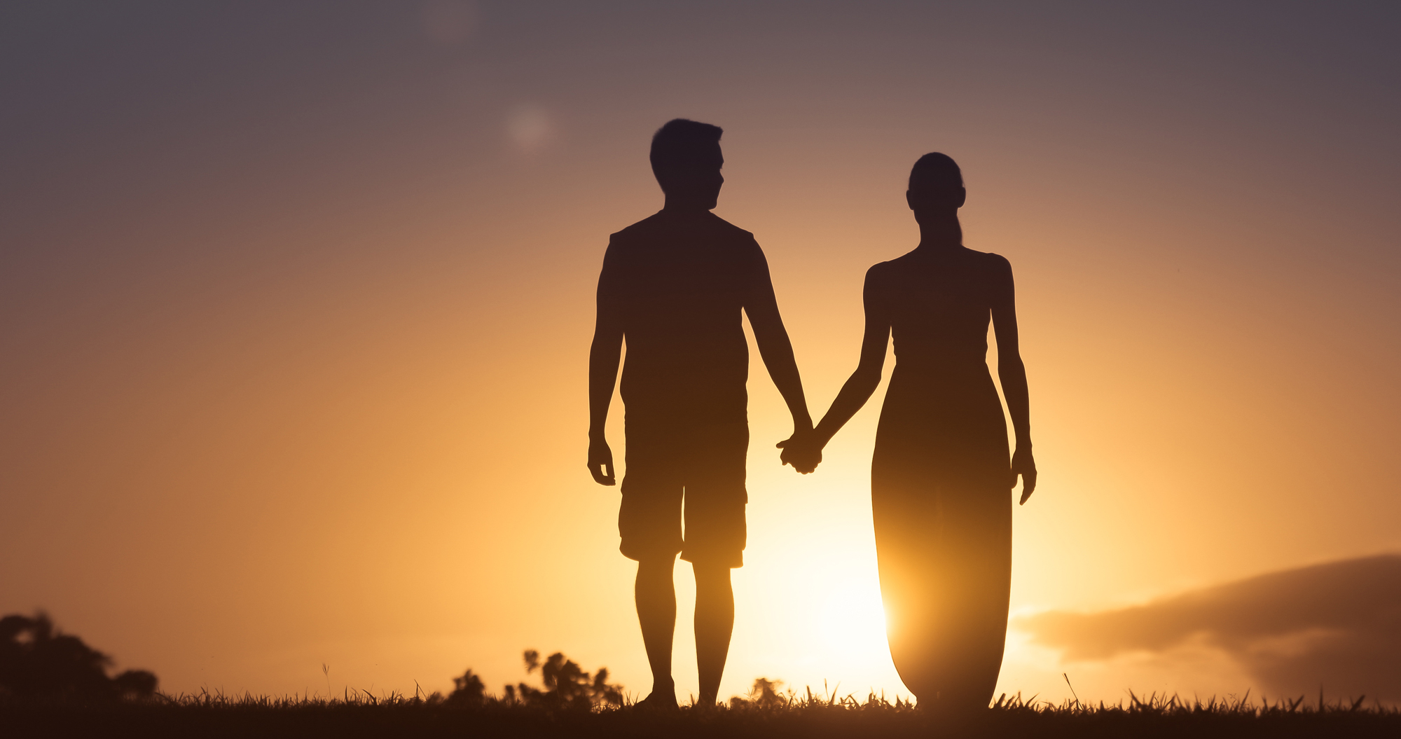 Man and woman holding hands walking into the sunset